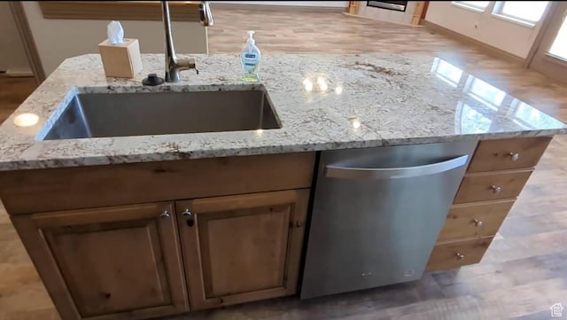 kitchen view of a sink, stainless steel dishwasher, light stone counters, and baseboards