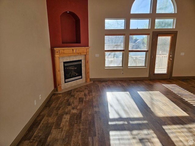 unfurnished living room featuring dark wood-type flooring, baseboards, a tiled fireplace, and a towering ceiling