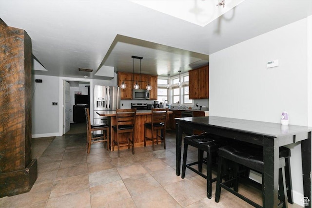 9 W Cedar Ln, Franklin, ID 83237 - kitchen featuring stainless steel appliances, decorative light fixtures, a breakfast bar area, baseboards, and brown cabinetry