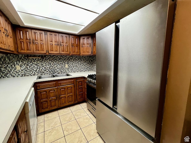 kitchen with stainless steel appliances, a sink, tasteful backsplash, light tile patterned flooring, and light countertops