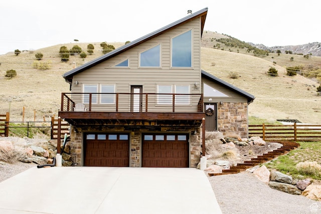 view of front of home with a mountain view, stone siding, fence, concrete driveway, and an attached garage