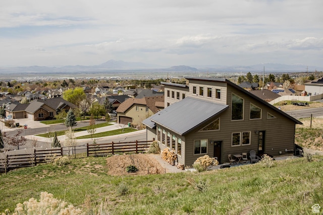 rear view of property featuring fence, a mountain view, a residential view, and metal roof