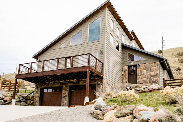 exterior space featuring stone siding, an attached garage, fence, and a deck
