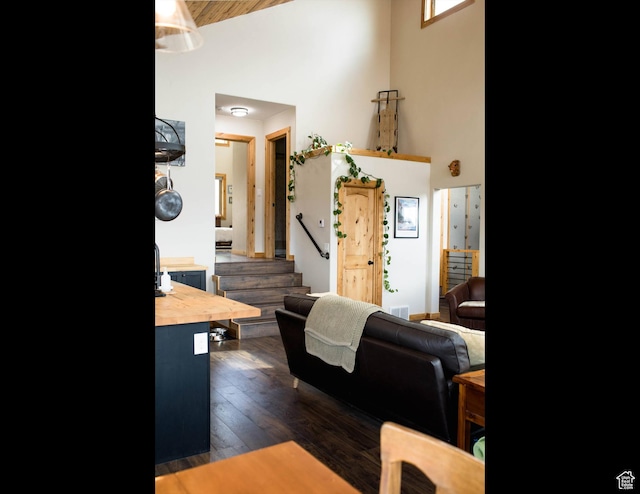 living area featuring dark wood-type flooring, stairs, and high vaulted ceiling