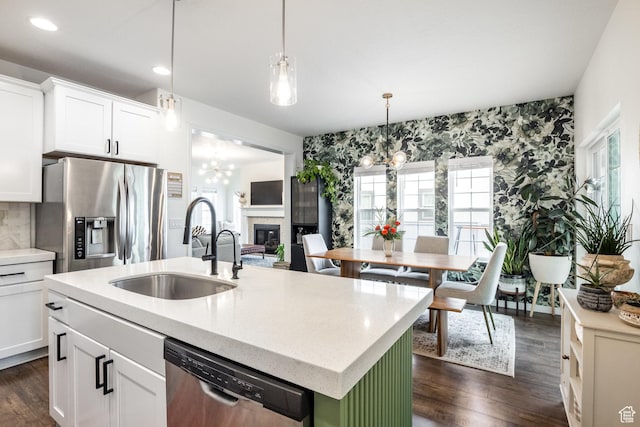 kitchen with stainless steel appliances, a sink, a glass covered fireplace, an inviting chandelier, and an island with sink