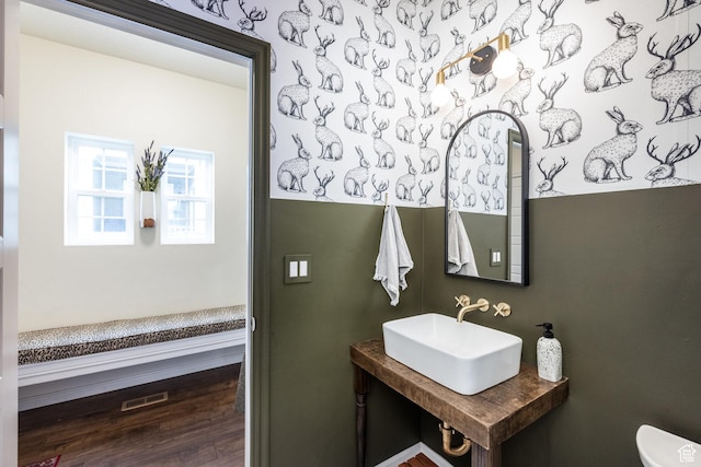 half bath with wood finished floors, visible vents, a sink, and toilet