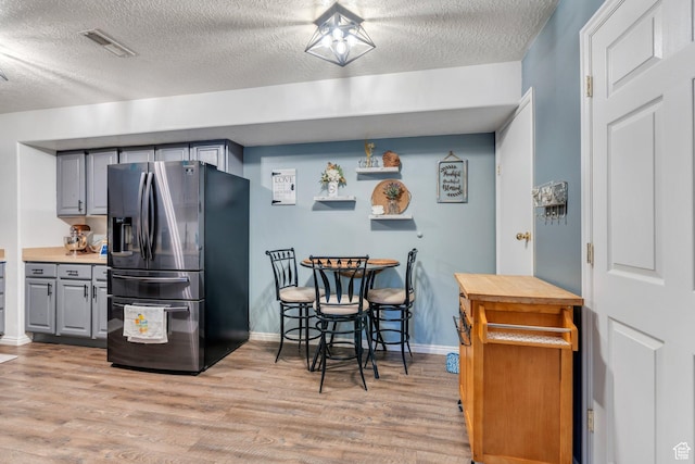 kitchen with a textured ceiling, light wood-type flooring, stainless steel refrigerator with ice dispenser, gray cabinetry, and visible vents