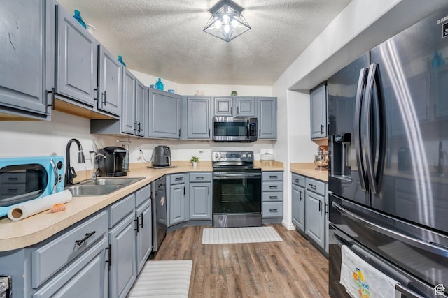 kitchen featuring a sink, stainless steel microwave, fridge with ice dispenser, gray cabinetry, and electric range oven