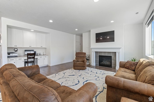 living area featuring built in desk, a fireplace, dark wood finished floors, baseboards, and recessed lighting
