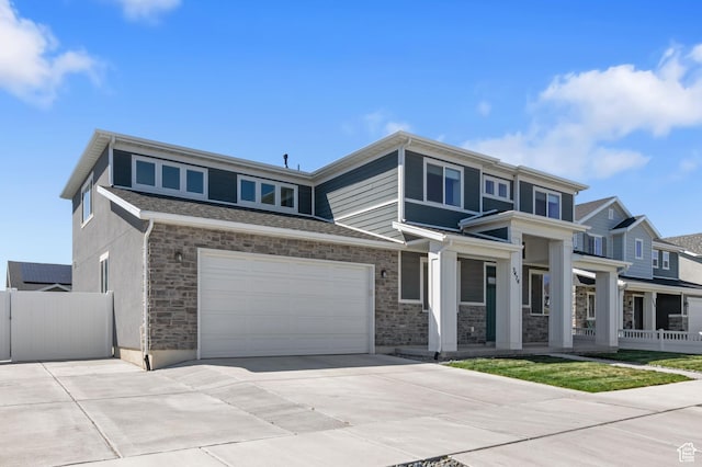prairie-style home featuring concrete driveway, stone siding, covered porch, fence, and a garage