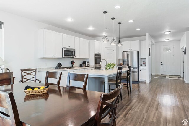 kitchen with white cabinets, stainless steel appliances, light countertops, wood finished floors, and a breakfast bar area