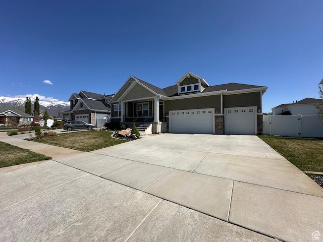 craftsman-style home with fence, a front lawn, concrete driveway, an attached garage, and stone siding