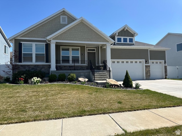 craftsman-style home with a front lawn, stone siding, covered porch, concrete driveway, and a garage