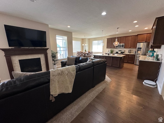 living area featuring dark wood-style floors, a textured ceiling, recessed lighting, a notable chandelier, and a fireplace