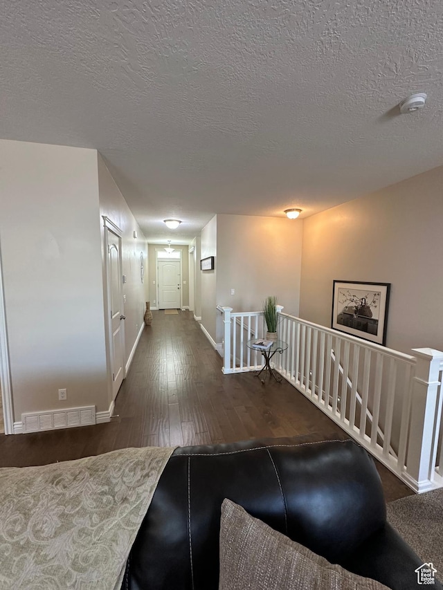 hallway with an upstairs landing, a textured ceiling, wood-type flooring, baseboards, and visible vents