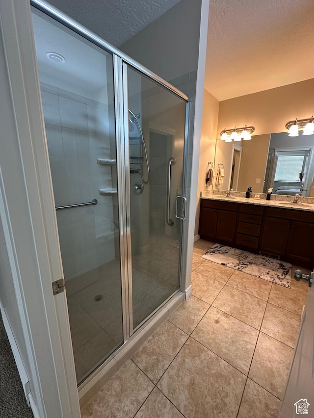 full bathroom featuring a sink, a textured ceiling, double vanity, a stall shower, and tile patterned flooring