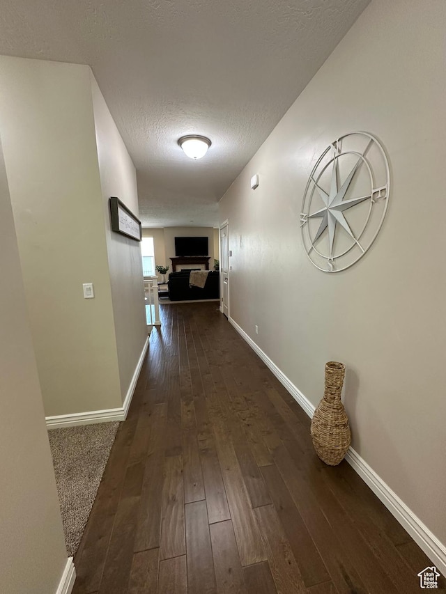 hallway featuring baseboards, dark wood-type flooring, and a textured ceiling