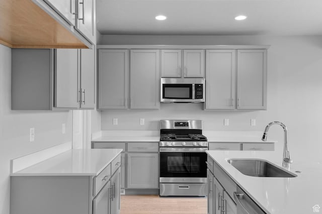kitchen with light countertops, appliances with stainless steel finishes, a sink, and gray cabinetry