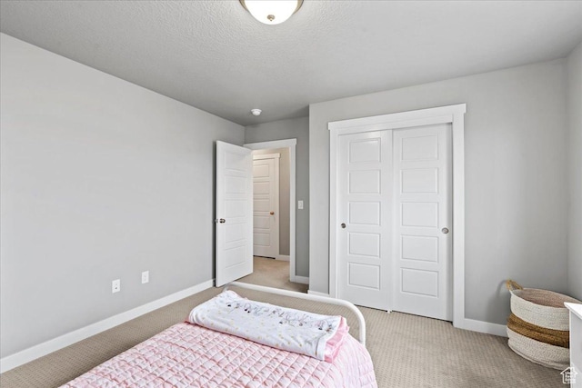 bedroom featuring light carpet, baseboards, a textured ceiling, and a closet