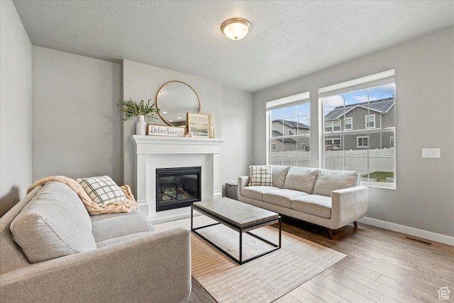living area featuring a textured ceiling, visible vents, baseboards, a glass covered fireplace, and hardwood / wood-style flooring