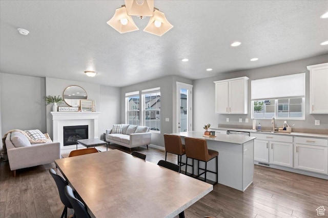 kitchen featuring a center island, a sink, open floor plan, white cabinetry, and wood finished floors