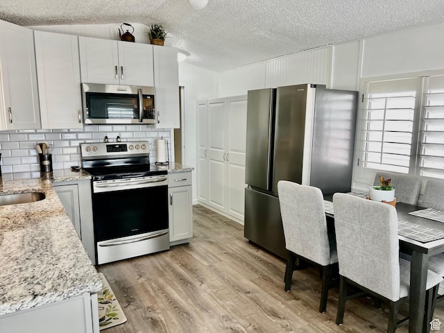 1150 W Red Hills Pkwy Unit 113, Washington, UT 84780 - kitchen featuring stainless steel appliances, a textured ceiling, light wood-style floors, backsplash, and light stone countertops