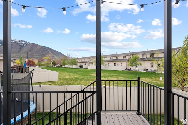 wooden deck with a fenced backyard, a residential view, a lawn, a mountain view, and a trampoline