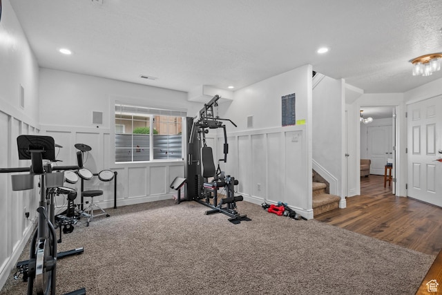 exercise room featuring a wainscoted wall, wood finished floors, visible vents, a decorative wall, and a textured ceiling