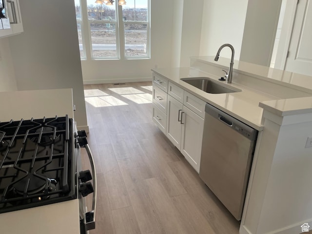 kitchen featuring range with gas stovetop, a sink, dishwasher, light wood-style flooring, and white cabinets