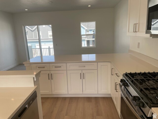 kitchen with light countertops, a peninsula, light wood-style flooring, appliances with stainless steel finishes, and white cabinetry