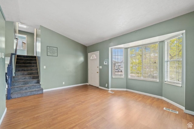 unfurnished living room featuring vaulted ceiling, wood finished floors, visible vents, baseboards, and stairs