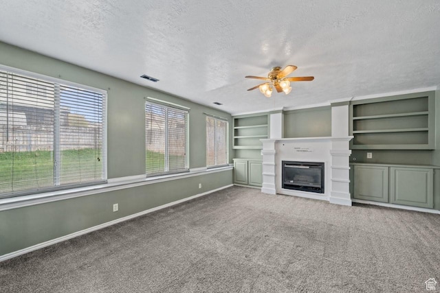 unfurnished living room with carpet, a ceiling fan, baseboards, a glass covered fireplace, and a textured ceiling