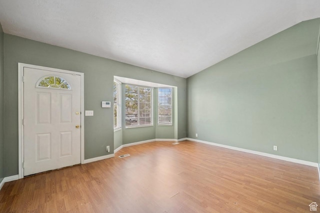 foyer featuring baseboards, lofted ceiling, visible vents, and light wood-style flooring
