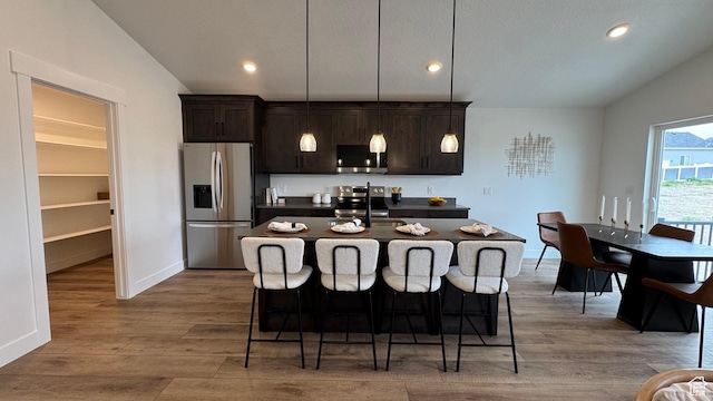 491 W 1860 N Unit 342, Tooele, UT 84074 - kitchen with dark countertops, dark brown cabinetry, a kitchen island with sink, stainless steel appliances, and a kitchen bar