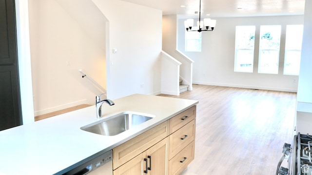 kitchen with an inviting chandelier, light countertops, a sink, light wood-style floors, and hanging light fixtures