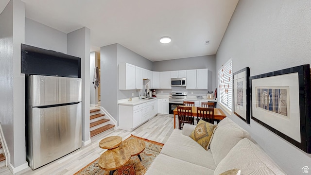 kitchen featuring light wood-style flooring, stainless steel appliances, light countertops, white cabinets, and baseboards