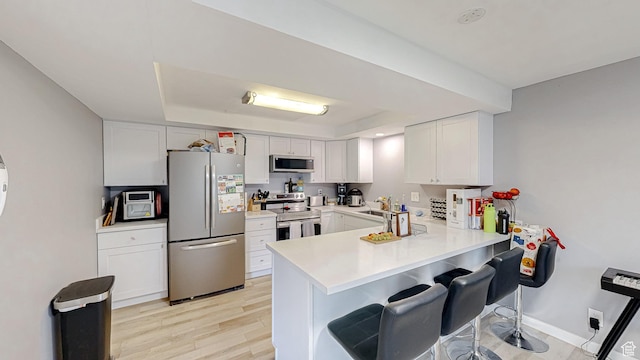 kitchen featuring white cabinets, light countertops, a peninsula, a kitchen bar, and appliances with stainless steel finishes