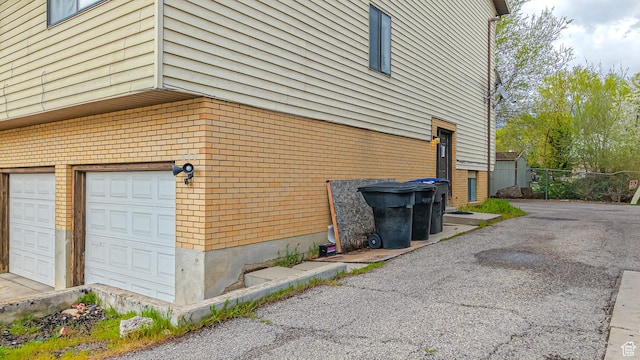 view of side of property featuring a garage, brick siding, and fence