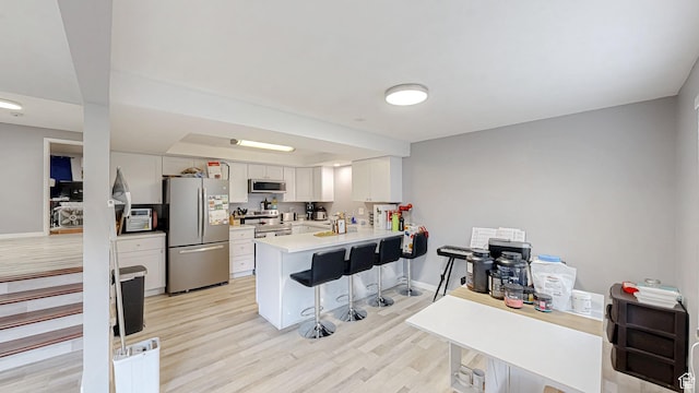 kitchen featuring light wood finished floors, stainless steel appliances, light countertops, a peninsula, and a breakfast bar area