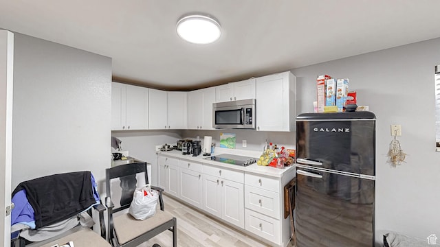 kitchen with white cabinets, light wood finished floors, light countertops, stainless steel microwave, and freestanding refrigerator