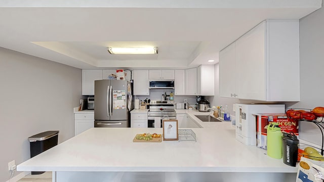 kitchen with a tray ceiling, light countertops, white cabinets, a peninsula, and appliances with stainless steel finishes
