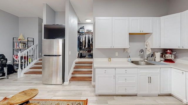 kitchen with white cabinets, a sink, light wood-type flooring, freestanding refrigerator, and light countertops