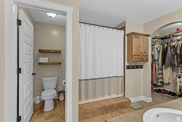 bathroom featuring a spacious closet, toilet, tile patterned flooring, and curtained shower