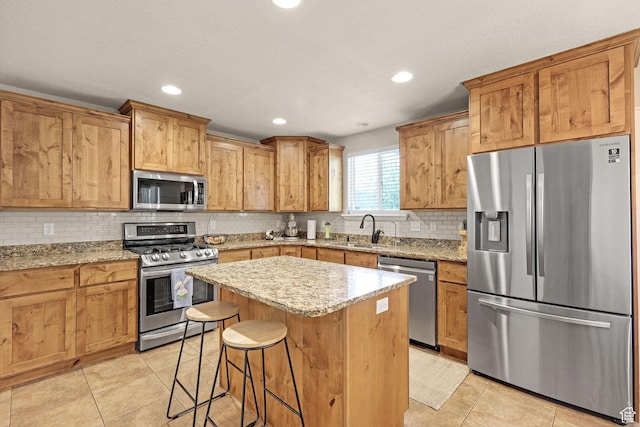kitchen with a kitchen breakfast bar, a sink, decorative backsplash, light tile patterned floors, and appliances with stainless steel finishes