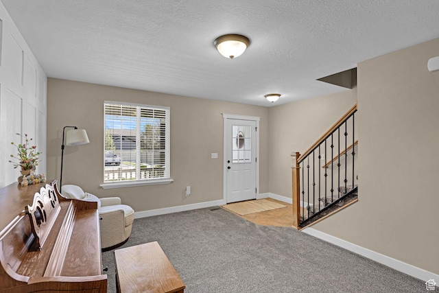 carpeted foyer with baseboards, stairs, and a textured ceiling