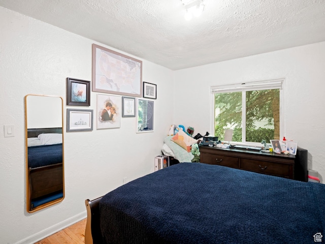 bedroom with baseboards, a textured ceiling, and light wood-type flooring