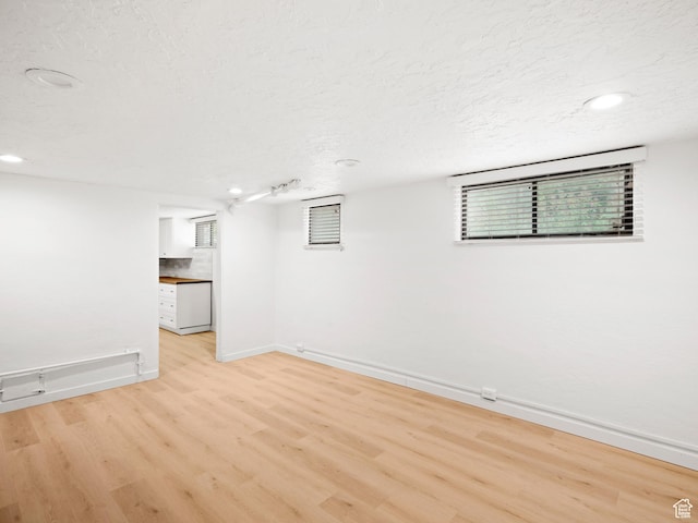 below grade area with light wood finished floors, baseboards, recessed lighting, and a textured ceiling