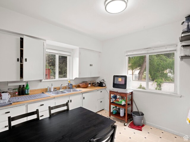kitchen with a sink, light floors, light countertops, white cabinets, and baseboards