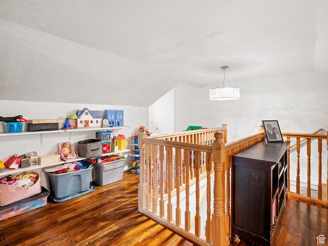recreation room featuring vaulted ceiling, wood finished floors, and a textured ceiling