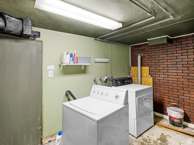 laundry room featuring a wood stove, laundry area, brick wall, and separate washer and dryer